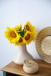 Bouquet of beautiful sunflowers, wicker basket and hat on table indoors