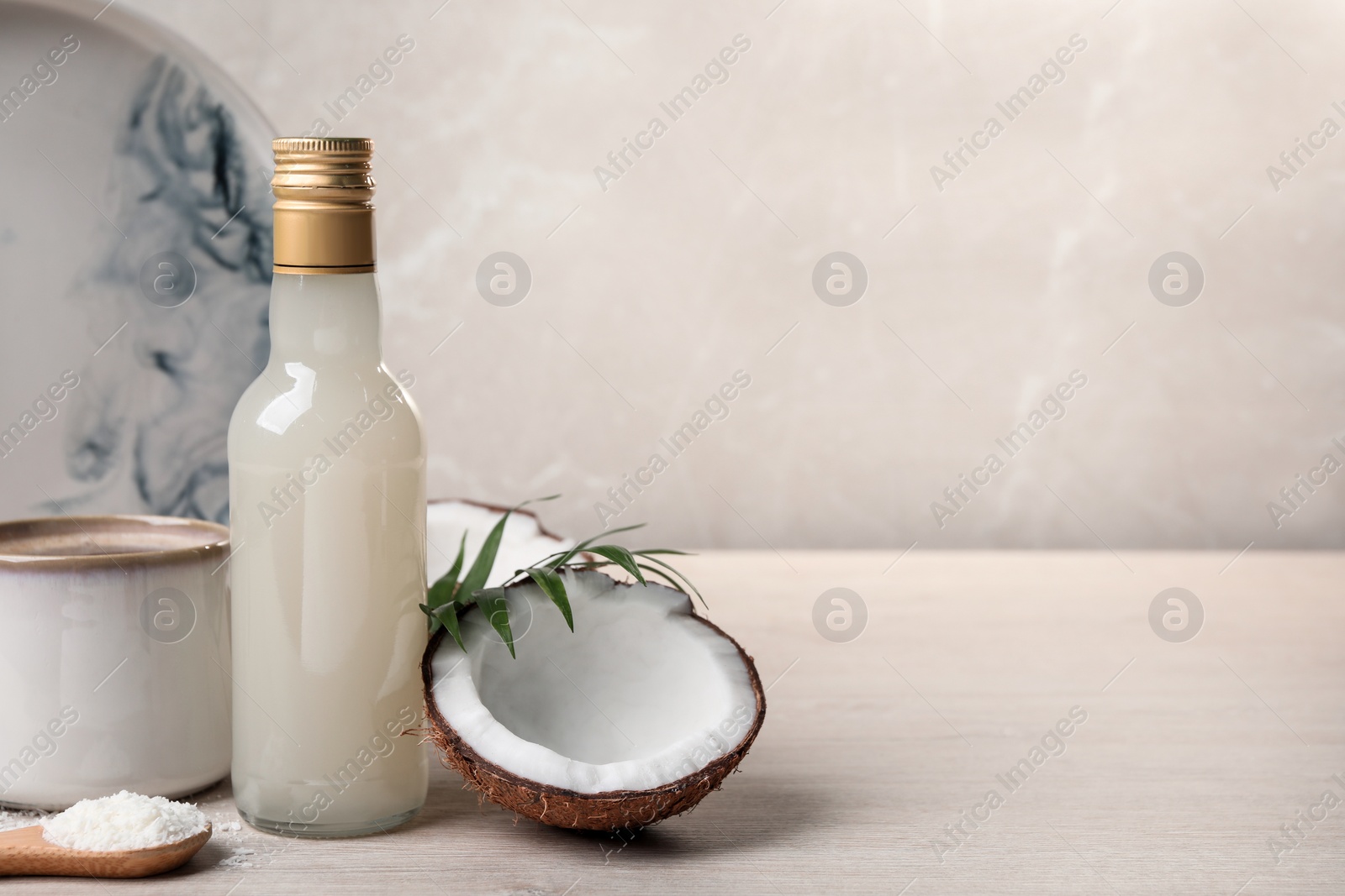 Photo of Bottle of delicious syrup, halves of coconut, flakes, cup of coffee and green leaves on white wooden table, space for text