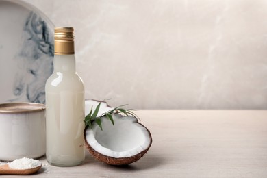 Photo of Bottle of delicious syrup, halves of coconut, flakes, cup of coffee and green leaves on white wooden table, space for text