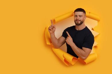 Photo of Special promotion. Young man pointing at something through hole in orange paper. Space for text