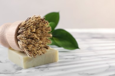 Photo of One cleaning brush and bar of soap on white marble table, closeup. Space for text