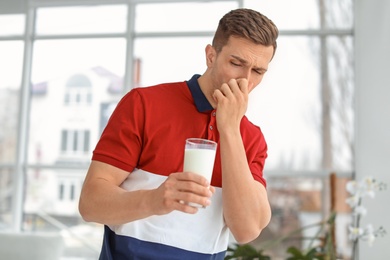 Photo of Young man with dairy allergy holding glass of milk indoors