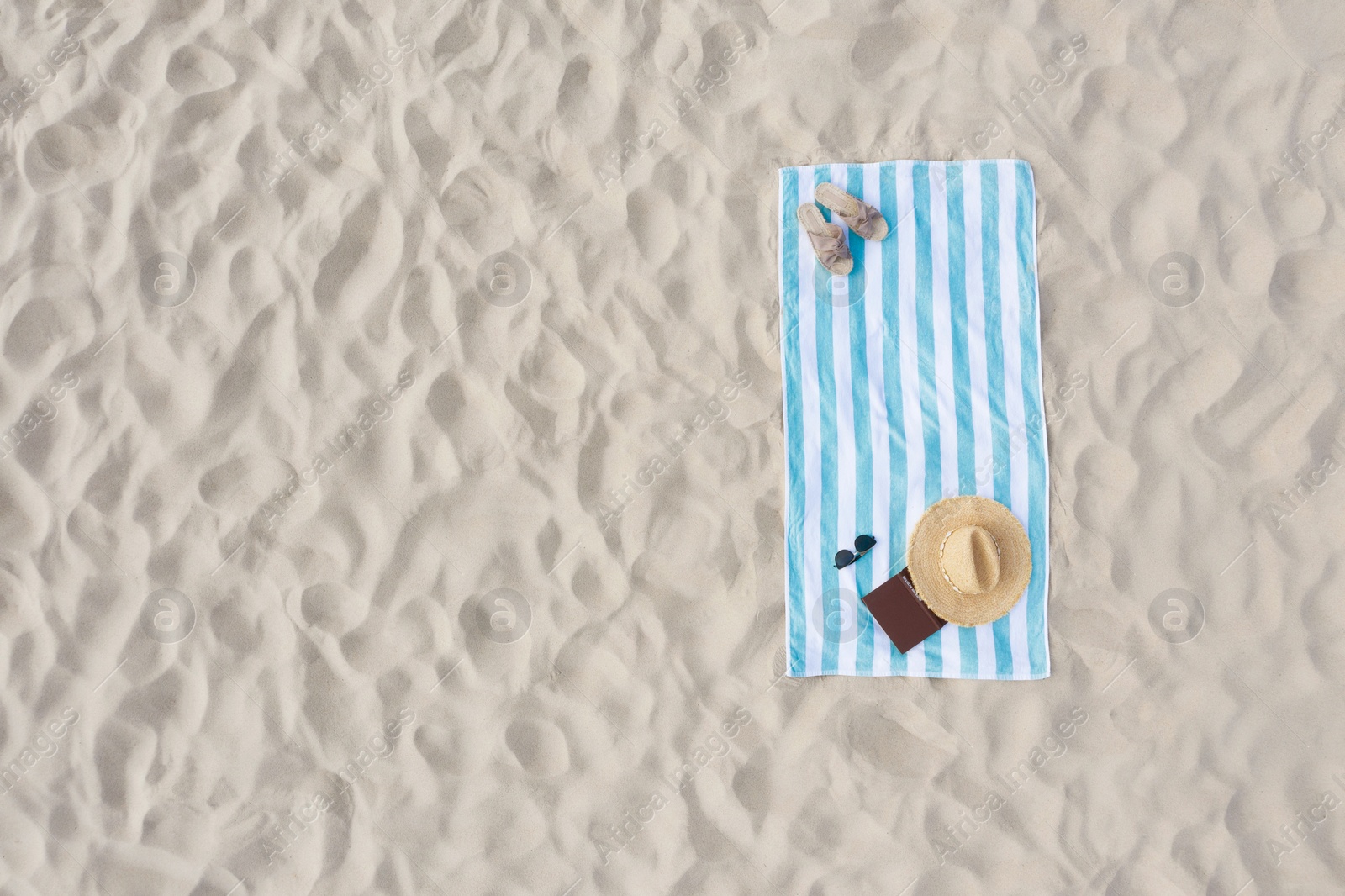 Image of Striped beach towel with straw hat, book, sunglasses and slippers on sand, aerial view. Space for text