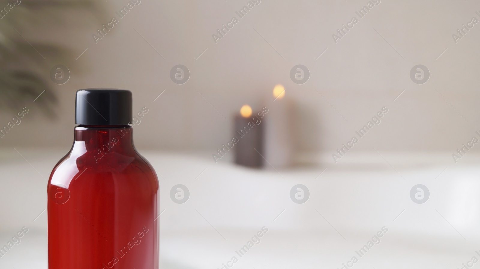 Photo of Red bottle of bath foam and candles indoors, closeup. Space for text
