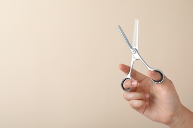 Photo of Hairdresser holding professional thinning scissors and space for text on beige background, closeup. Haircut tool