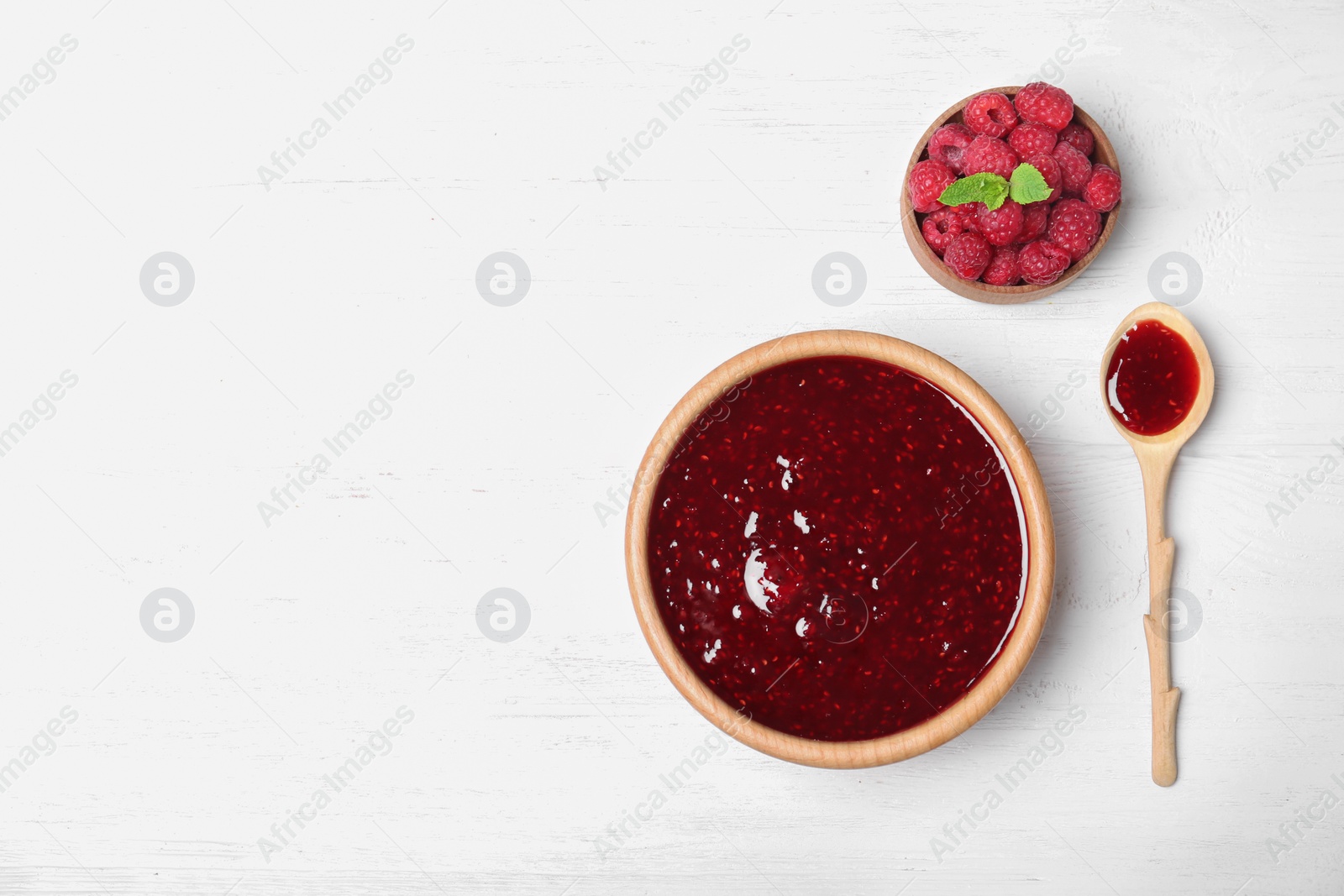 Photo of Bowl and spoon with delicious raspberry jam on wooden table, top view