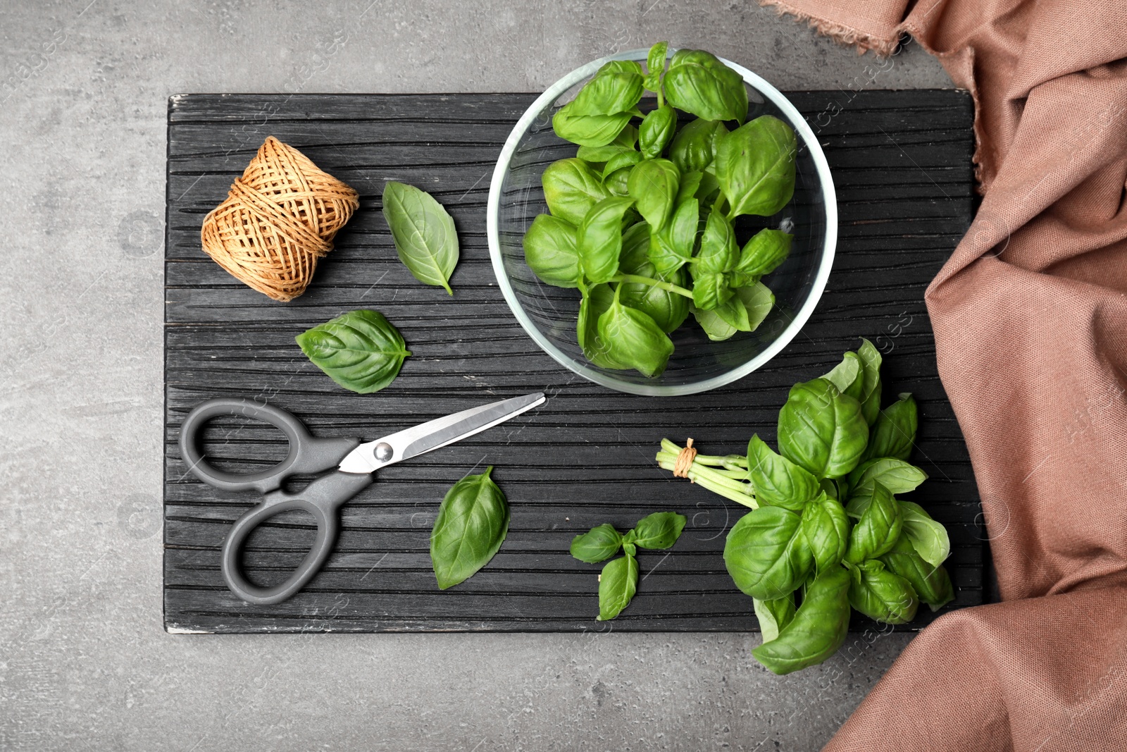 Photo of Board with fresh basil, scissors, rope and cloth on table, top view