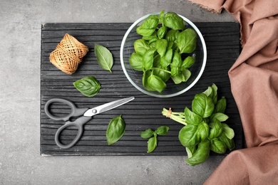 Board with fresh basil, scissors, rope and cloth on table, top view