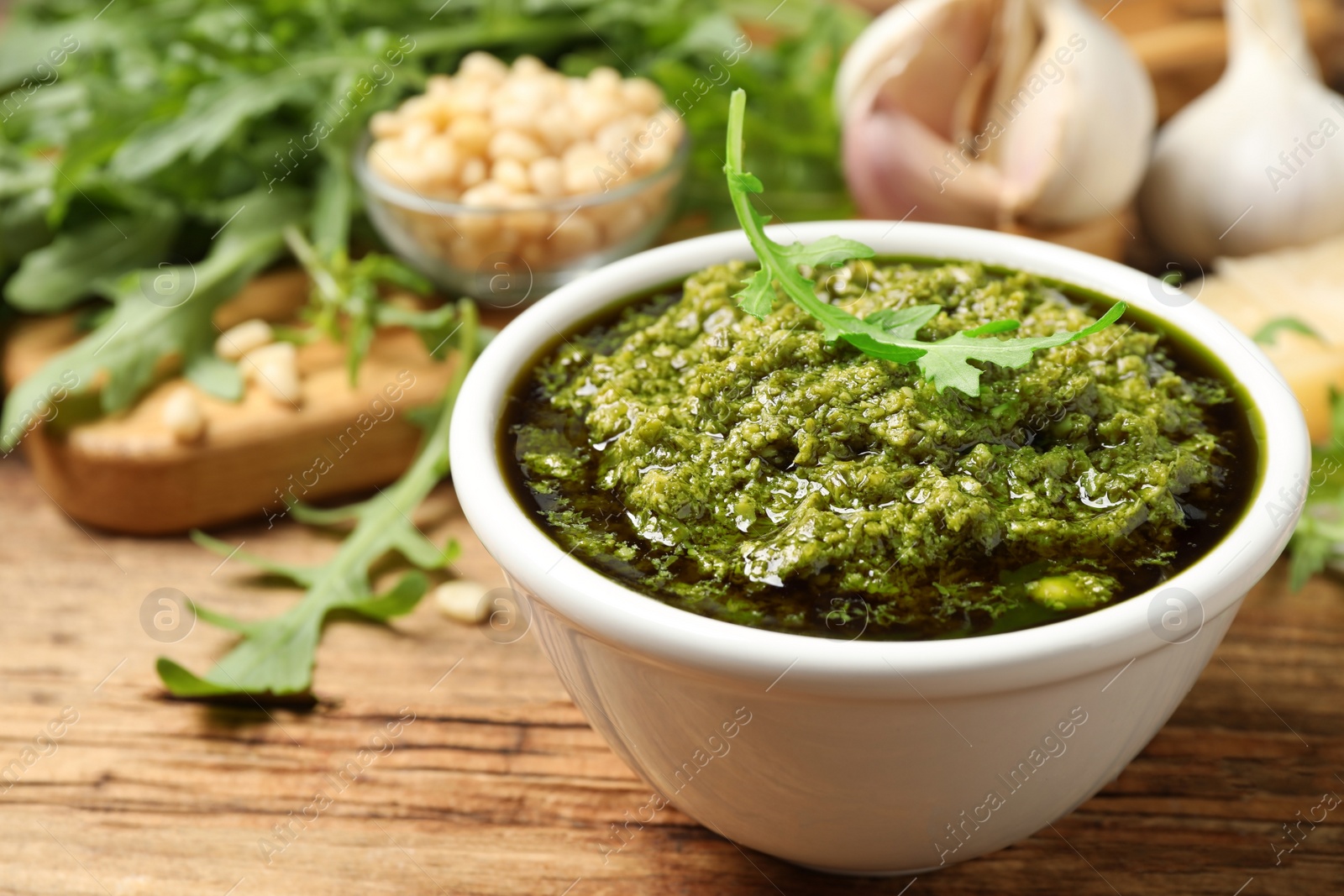 Photo of Bowl of tasty arugula pesto on wooden table, closeup