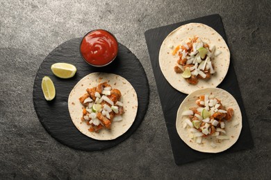 Photo of Delicious tacos with vegetables, meat and ketchup on grey textured table, flat lay