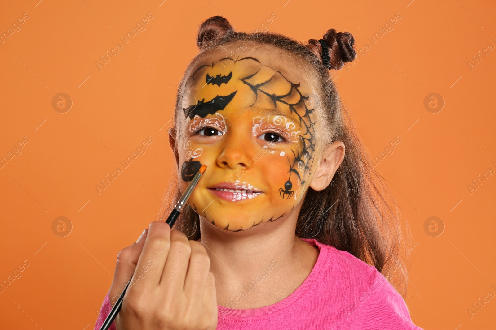 Photo of Artist painting face of little girl on orange background