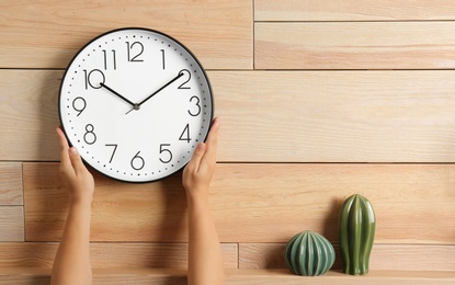 Photo of Woman touching clock on wooden wall, space for text. Time management