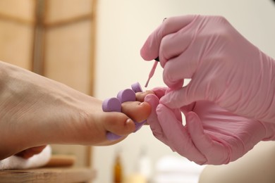 Professional pedicurist painting client`s toenails with polish in beauty salon, closeup