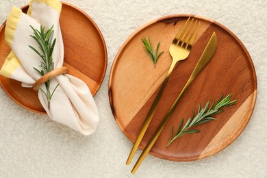 Photo of Stylish setting with cutlery, napkin, rosemary and plates on light textured table, flat lay