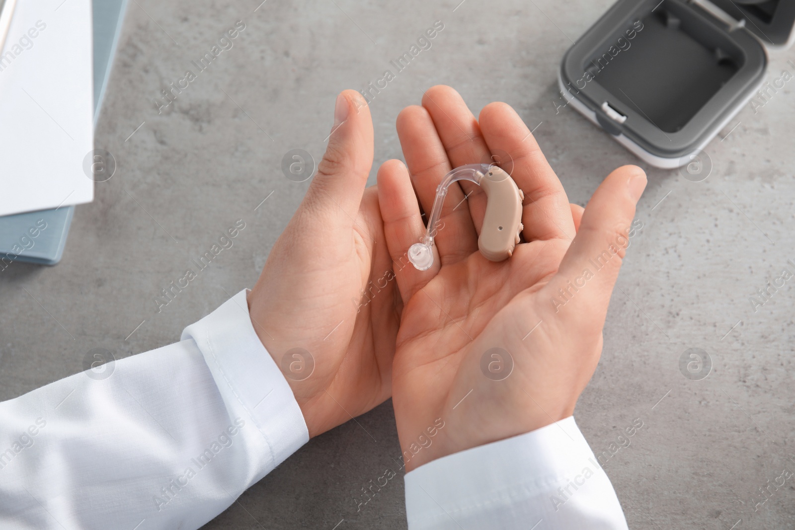 Photo of Doctor holding hearing aid at table, closeup. Medical device