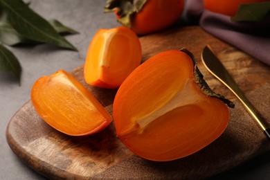 Photo of Pieces of delicious ripe persimmons and knife on wooden board, closeup