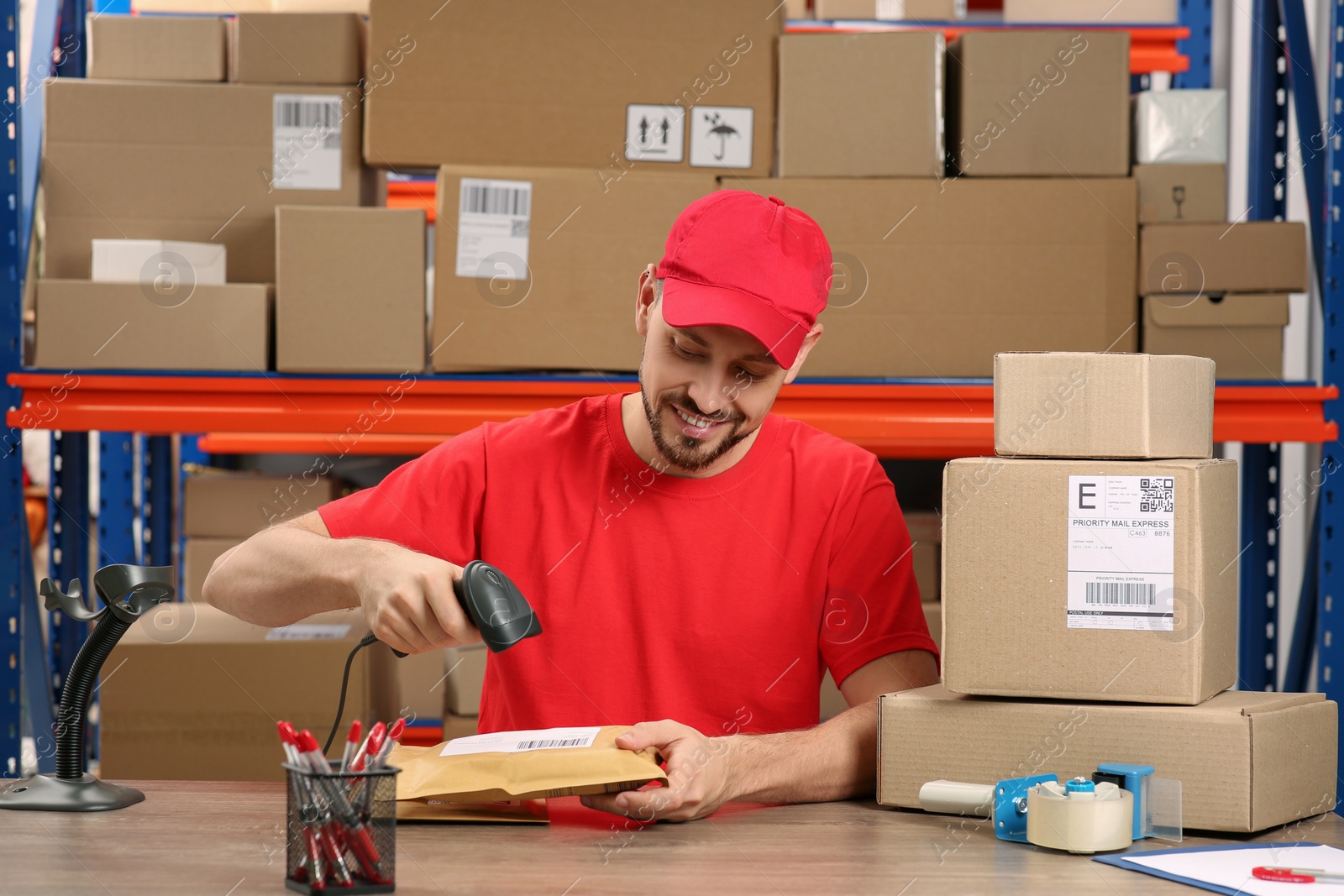 Photo of Post office worker with scanner reading parcel barcode at counter indoors