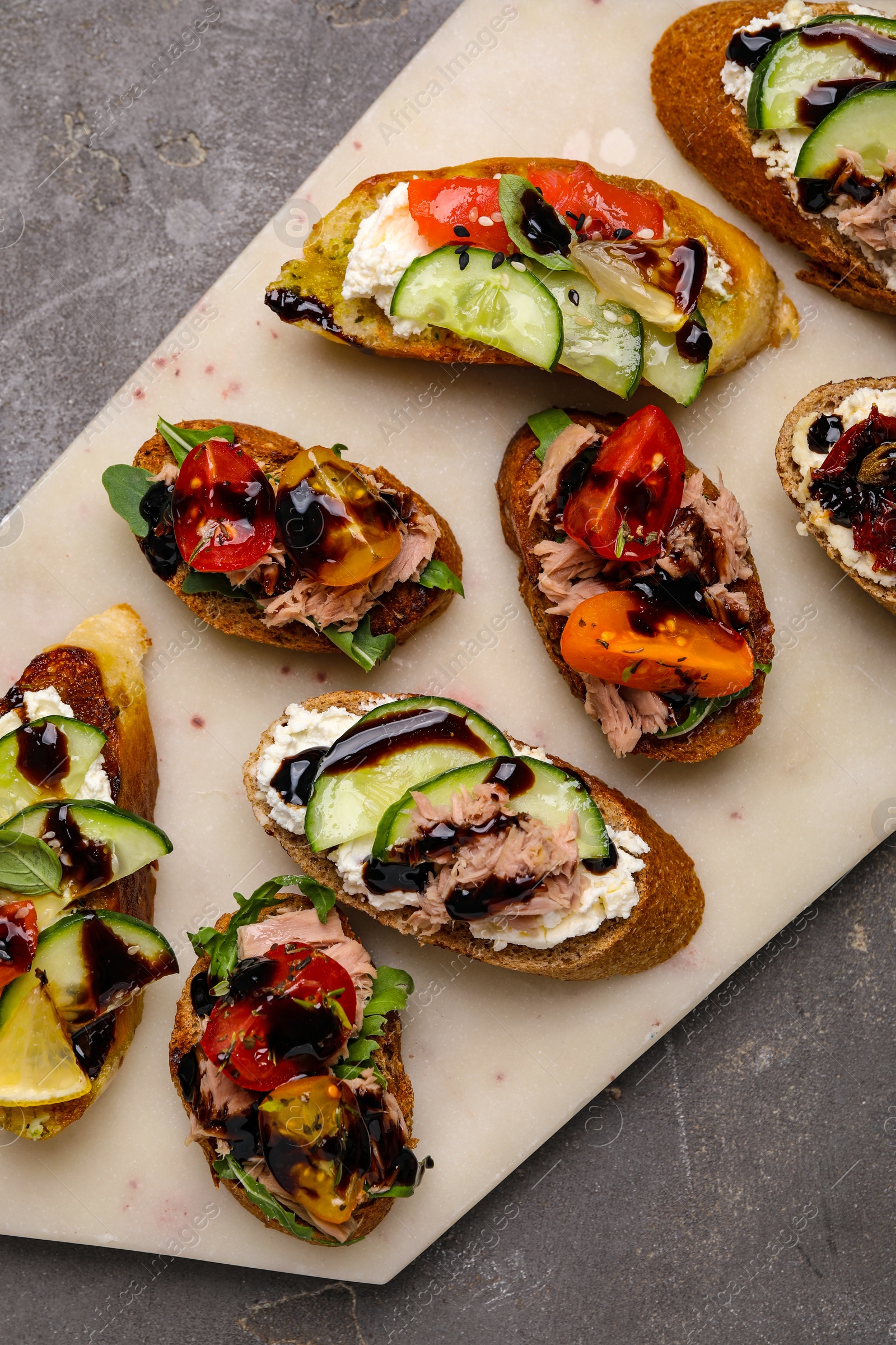 Photo of Delicious bruschettas with balsamic vinegar and different toppings on grey textured table, top view