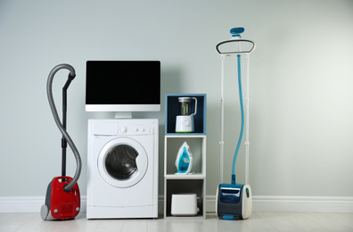 Photo of Modern vacuum cleaner and different household appliances near light wall indoors