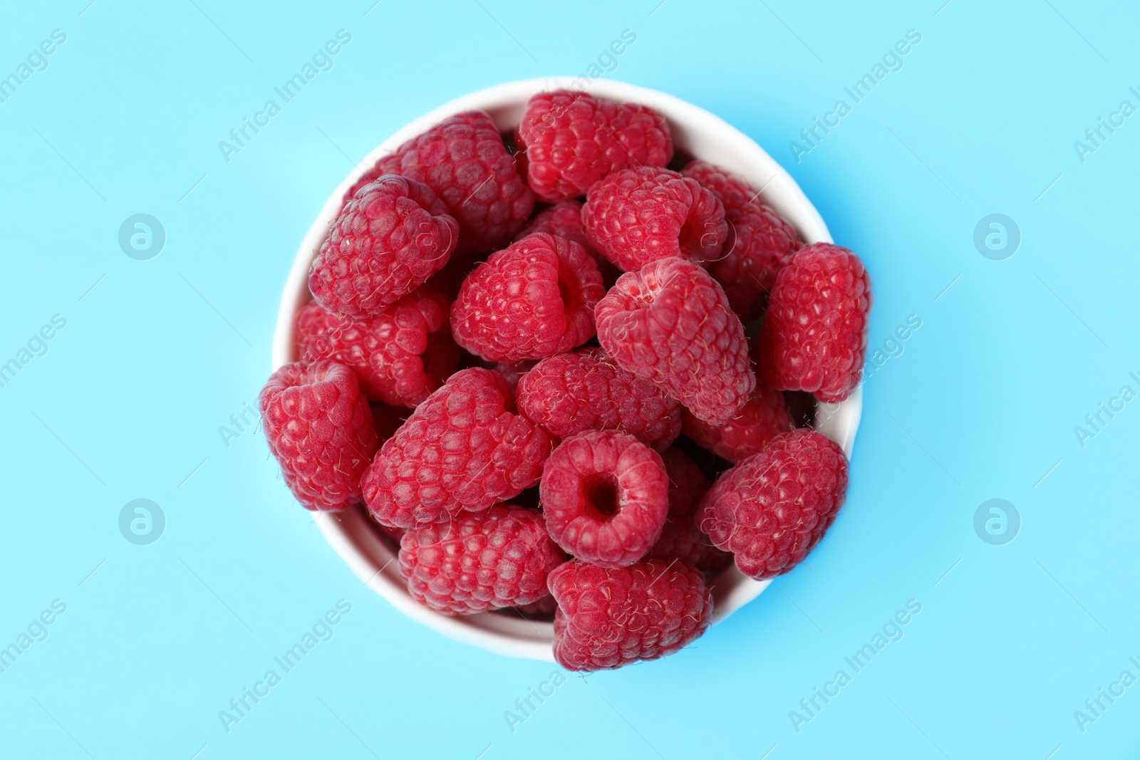 Photo of Bowl of delicious ripe raspberries on blue background, top view