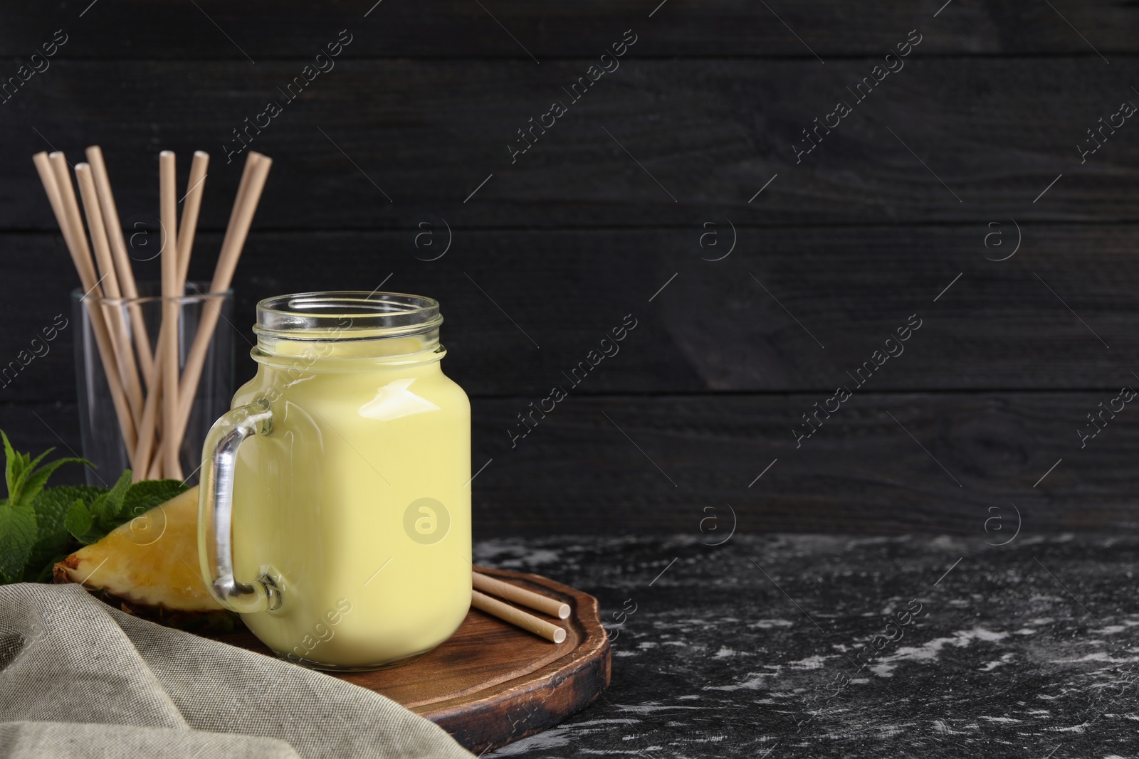 Photo of Tasty pineapple smoothie, slice of fruit and straws on dark textured table. Space for text