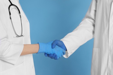 Photo of Doctors shaking hands on light blue background, closeup