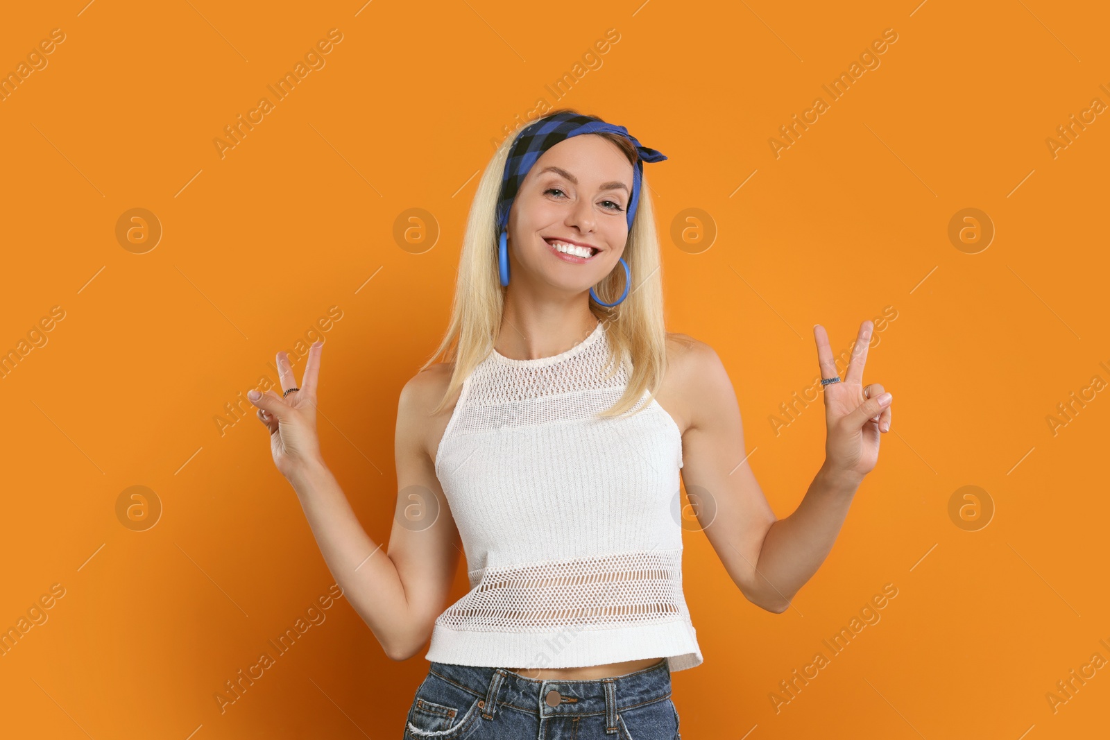 Photo of Smiling hippie woman showing peace signs on orange background