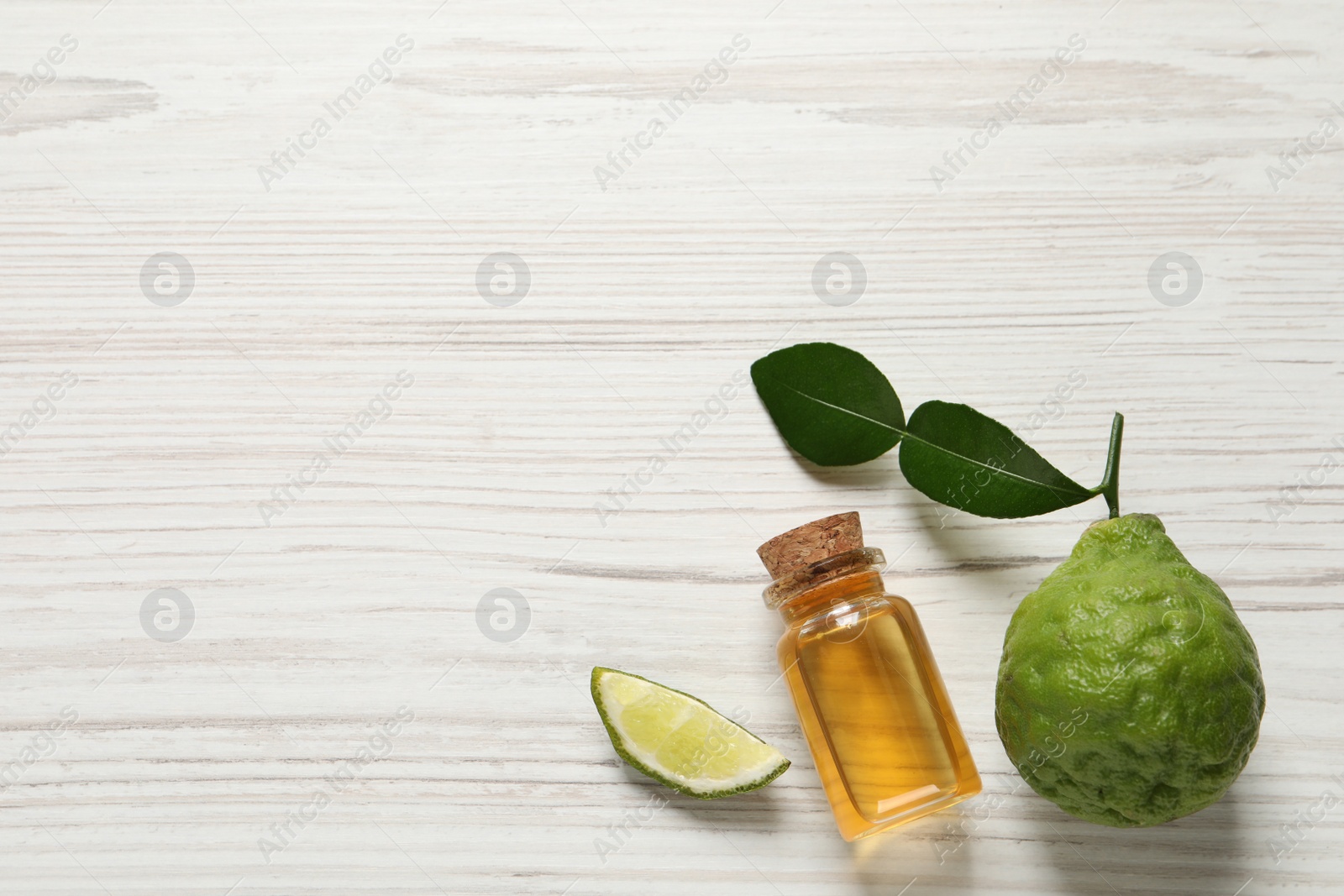 Photo of Glass bottle of bergamot essential oil and fresh fruit on white wooden table, flat lay. Space for text