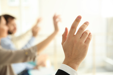 Photo of Young man raising hand to ask question at business training indoors, closeup