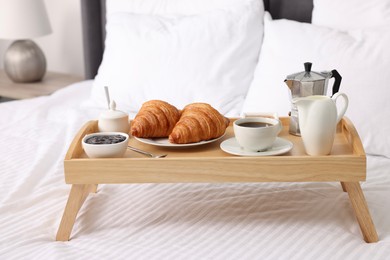 Photo of Wooden tray with tasty breakfast on bed at home