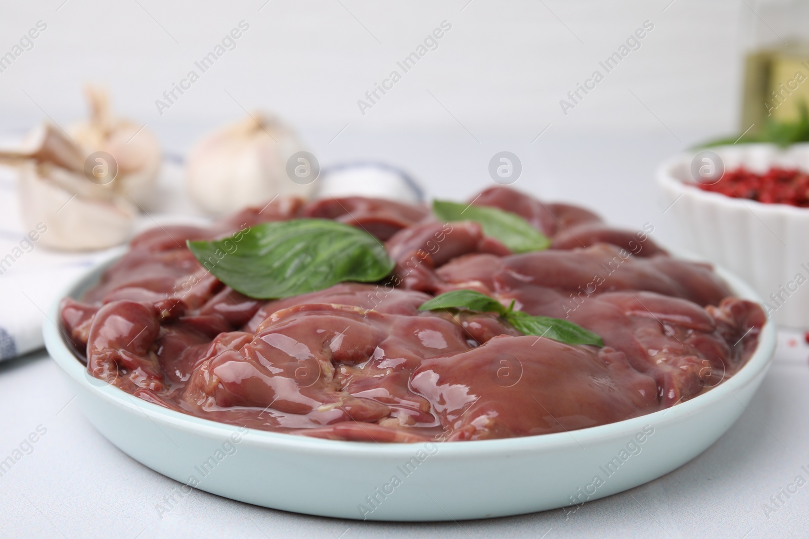 Photo of Plate of raw chicken liver with basil on white table, closeup