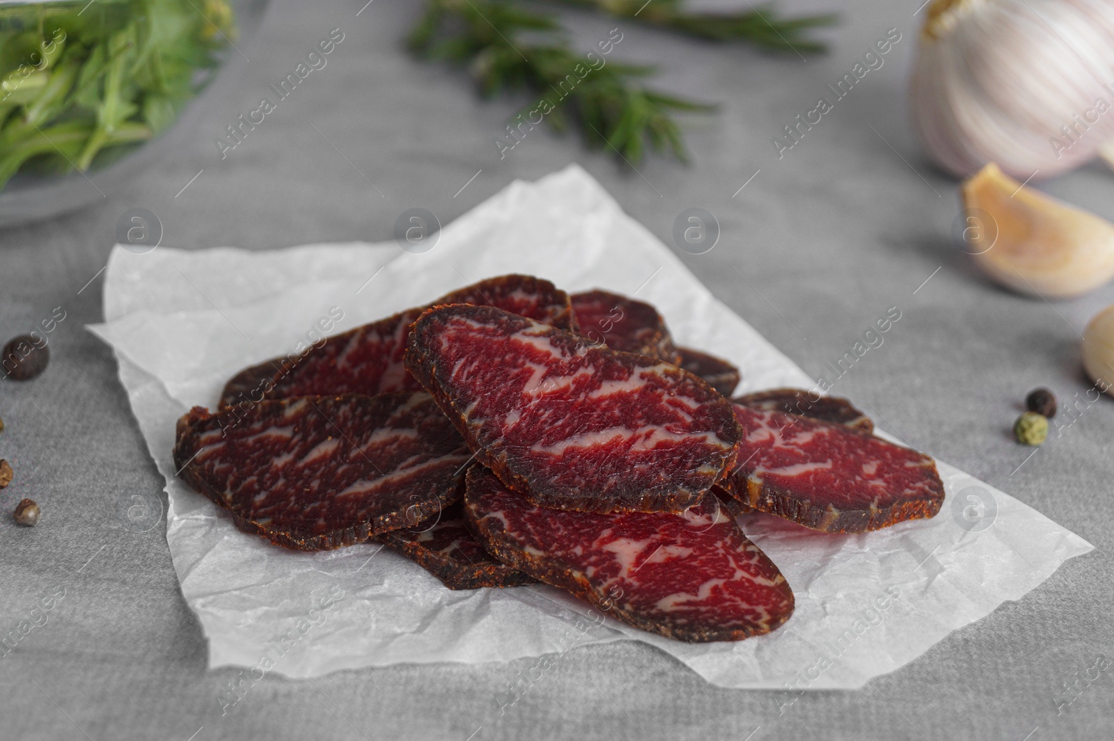 Photo of Slices of delicious beef jerky and spices on light grey table, closeup