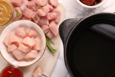 Photo of Fondue pot with oil, raw meat pieces, mustard and sauce on white marble table, flat lay