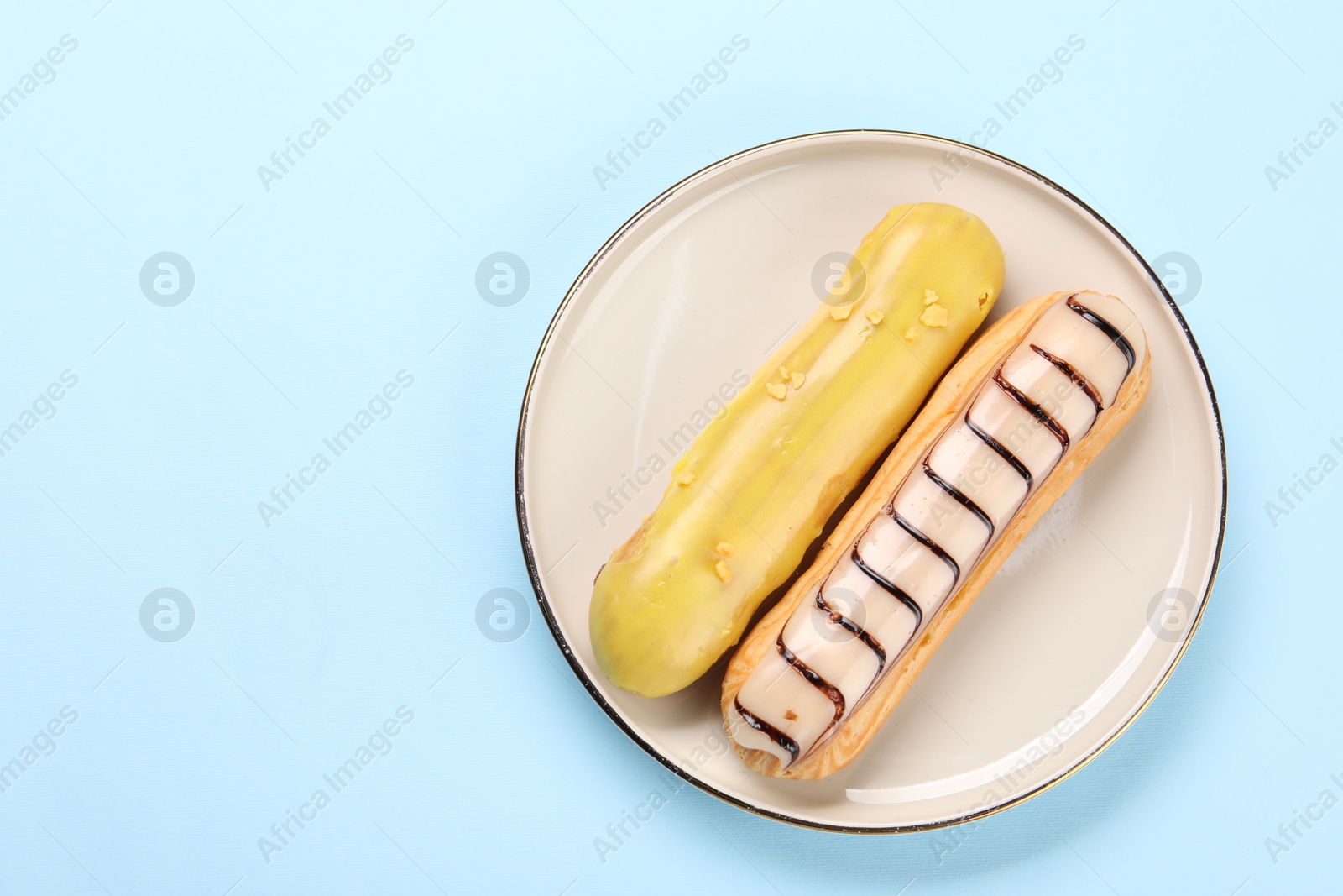 Photo of Delicious eclairs covered with glaze on light blue background, top view. Space for text