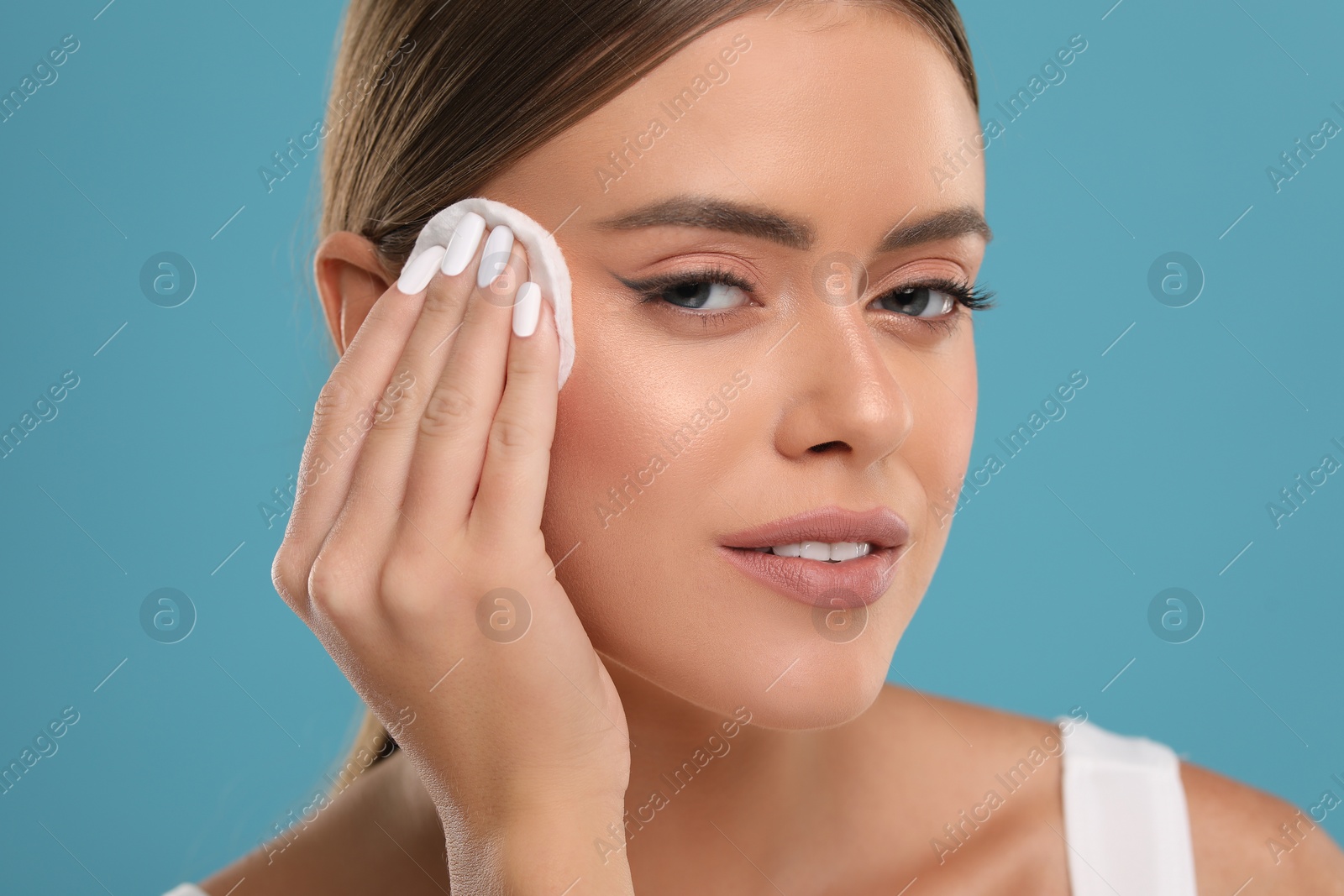 Photo of Beautiful woman removing makeup with cotton pad on light blue background, closeup