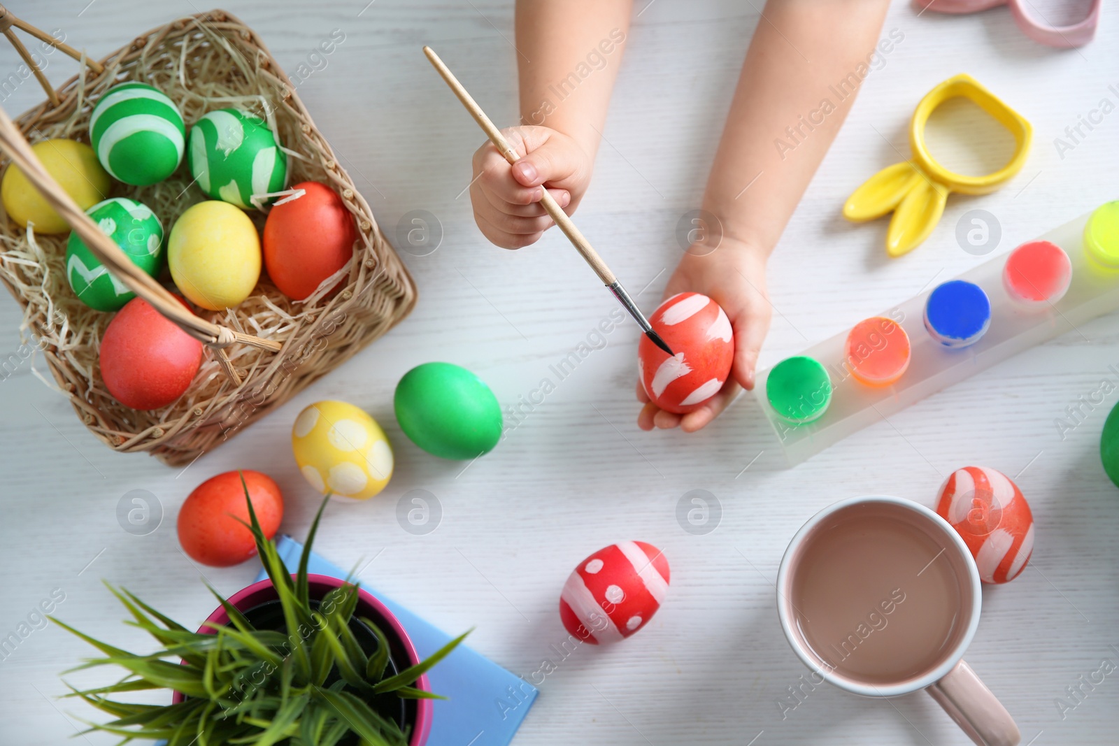 Photo of Little child painting Easter eggs on wooden background, top view