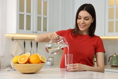 Young woman pouring water into glass from jug in kitchen