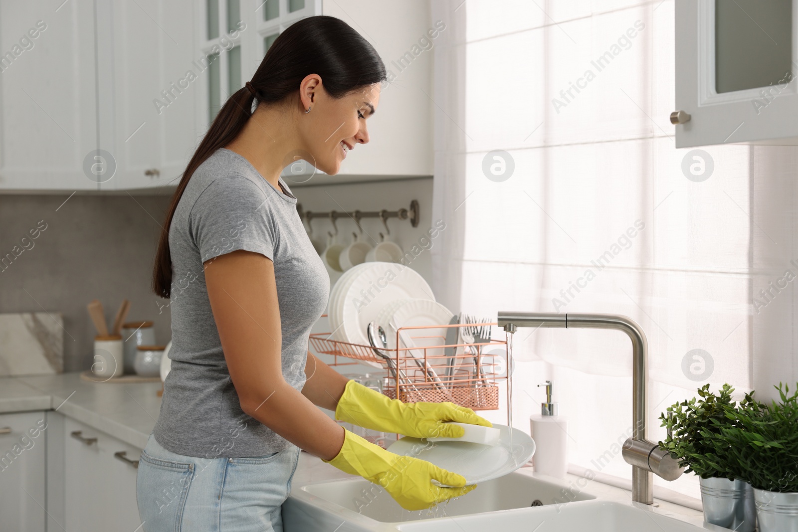 Photo of Happy woman washing plate at sink in kitchen