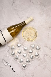 Photo of Heart made with delicious chocolate candies and champagne on white marble table, flat lay