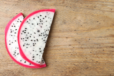Photo of Slices of delicious dragon fruit (pitahaya) on wooden table, flat lay. Space for text