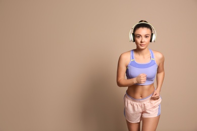 Young woman in sportswear with headphones running on beige background. Space for text