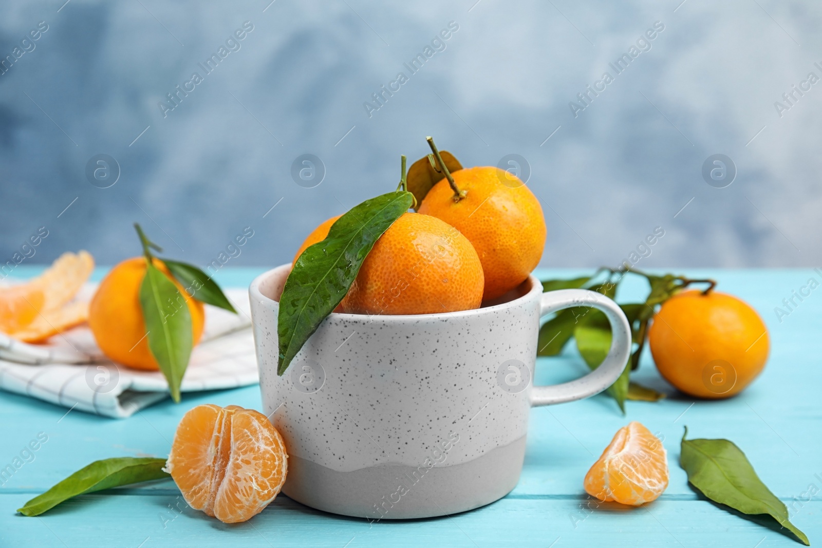 Photo of Fresh ripe tangerines with green leaves and mug on table