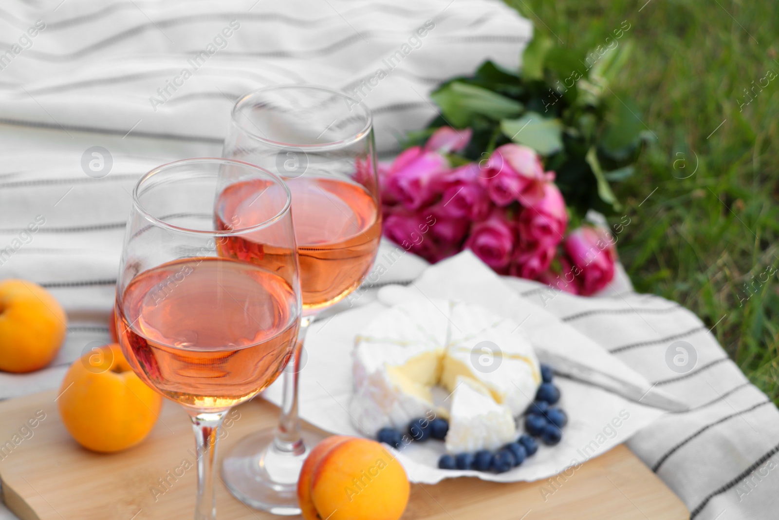 Photo of Glasses of delicious rose wine, flowers and food on picnic blanket outdoors