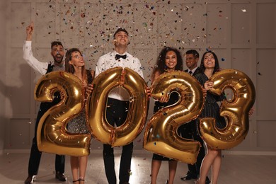 Photo of Happy friends with golden 2023 balloons indoors. New Year celebration