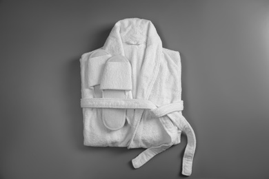 Photo of Clean folded bathrobe and slippers on grey background, top view