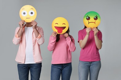 People covering faces with emoticons on grey background