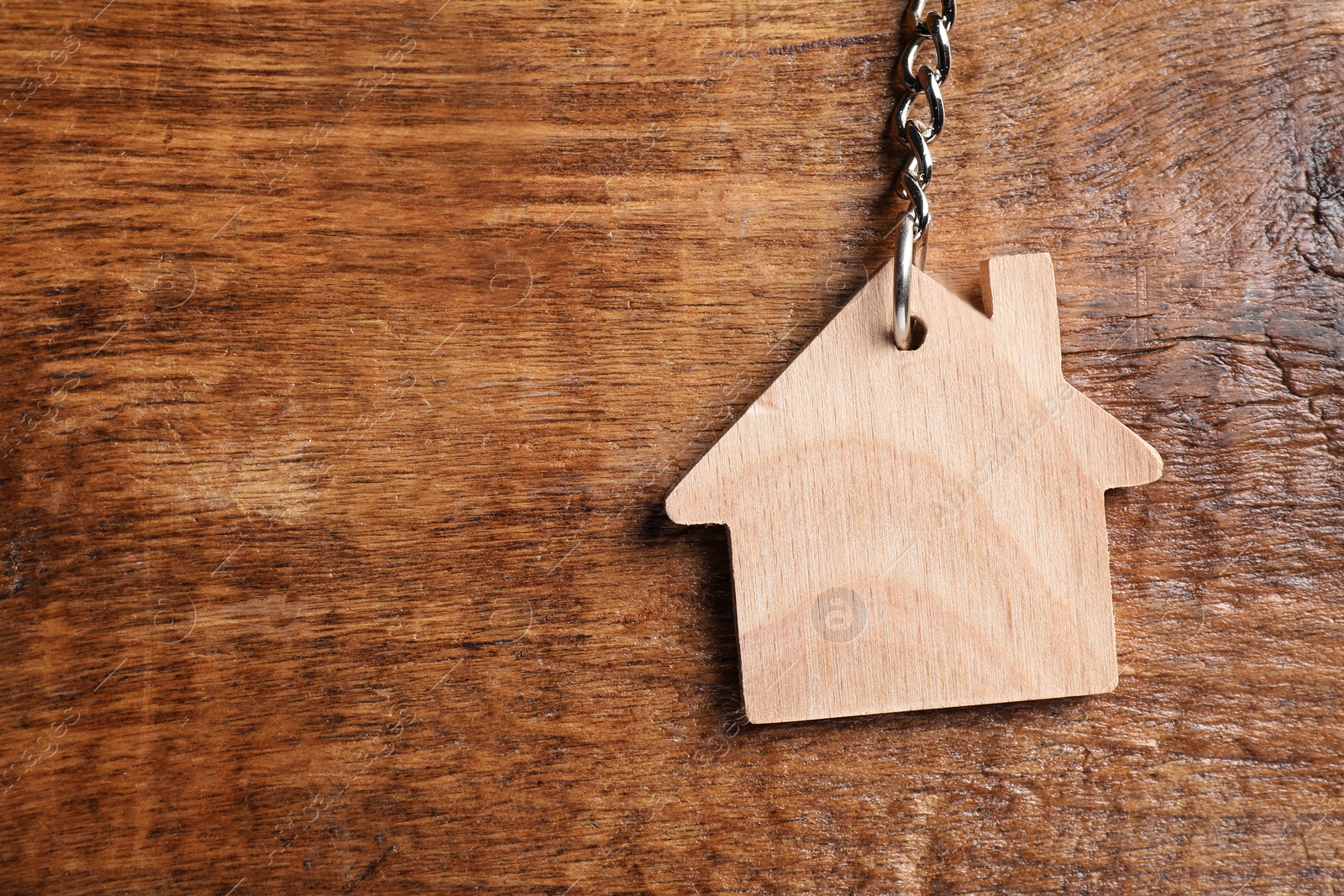 Photo of One keychain in shape of house on wooden table, top view. Space for text