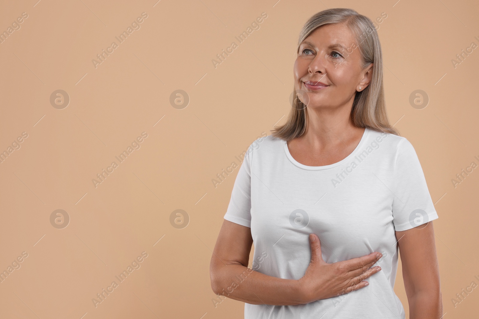 Photo of Beautiful senior woman doing breast self-examination on light brown background. Space for text