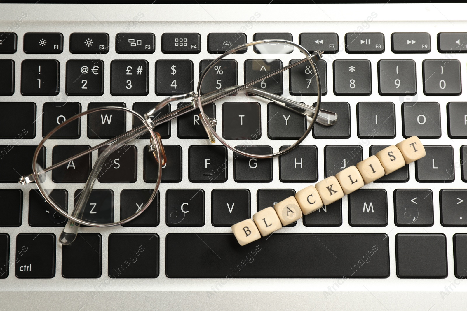 Photo of Wooden cubes with word Blacklist and glasses on laptop keyboard, top view