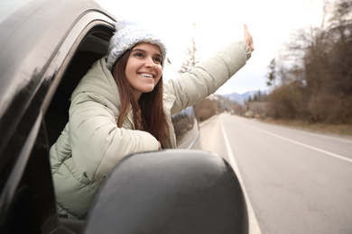 Happy woman leaning out of car window on road. Winter vacation